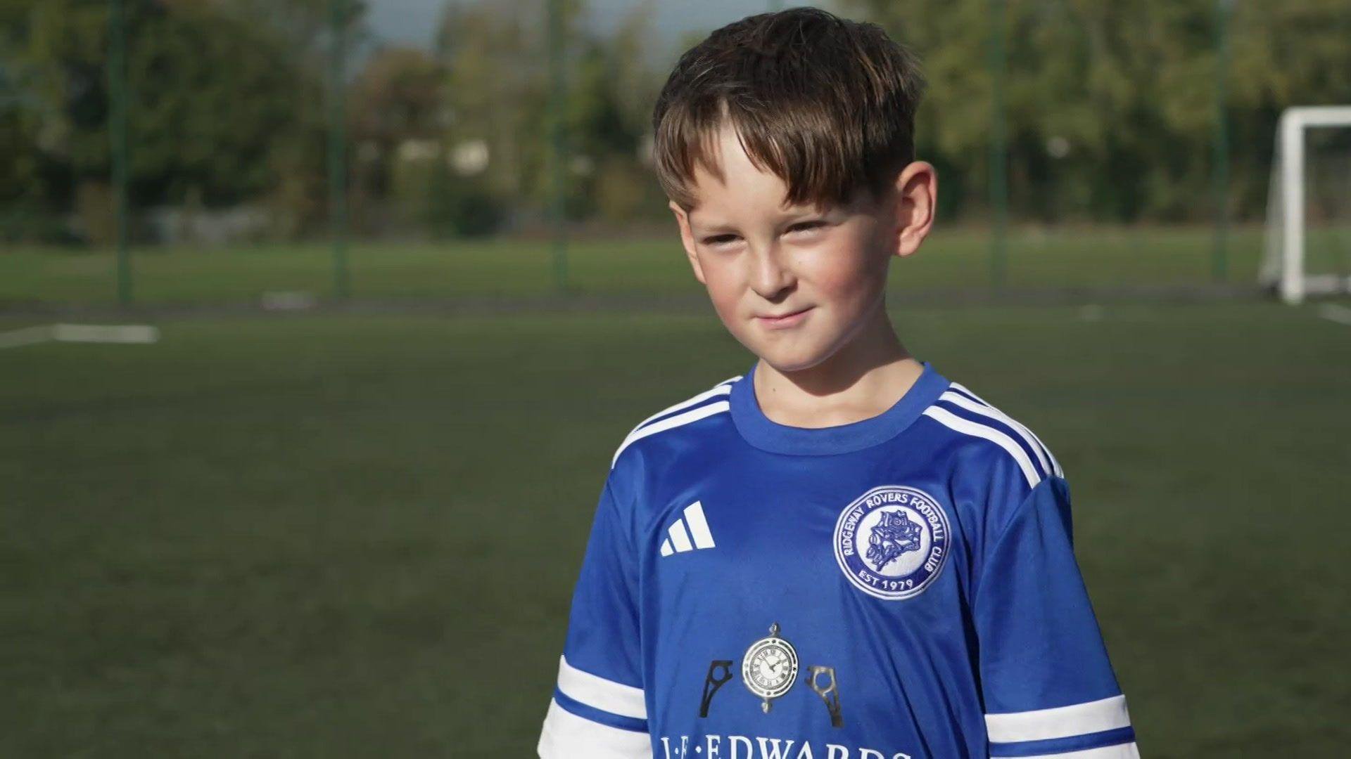 A boy with brown hair in a Ridgeway Rovers football top.