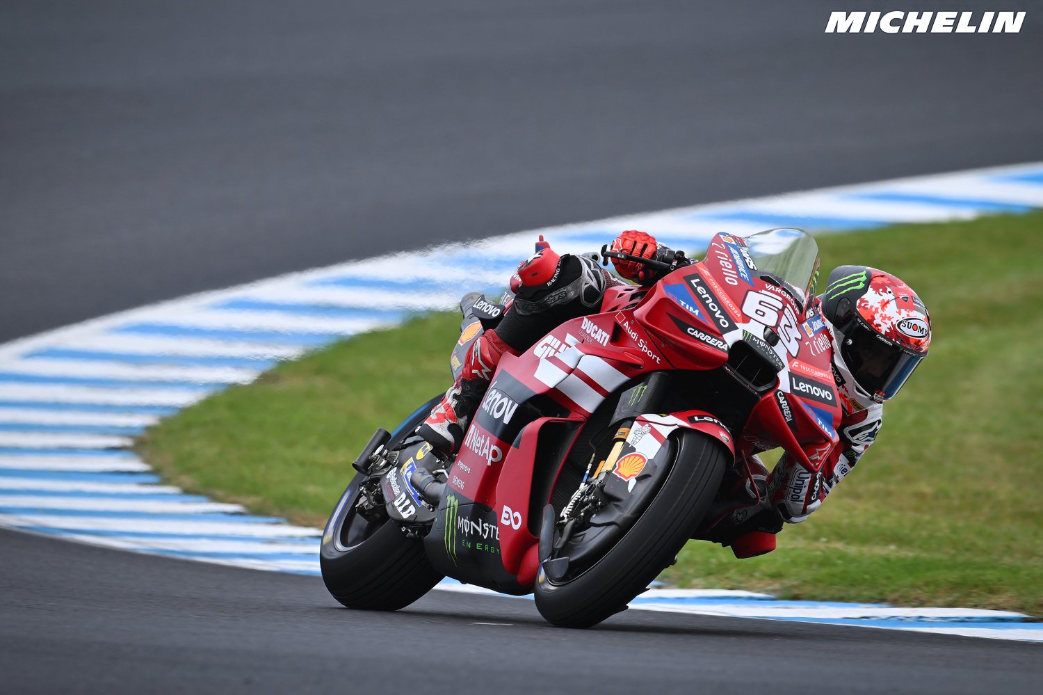 A rider in red Ducati Lenovo leathers and helmet leans through a corner on a red Ducati MotoGP bike at Phillip Island, Australia.