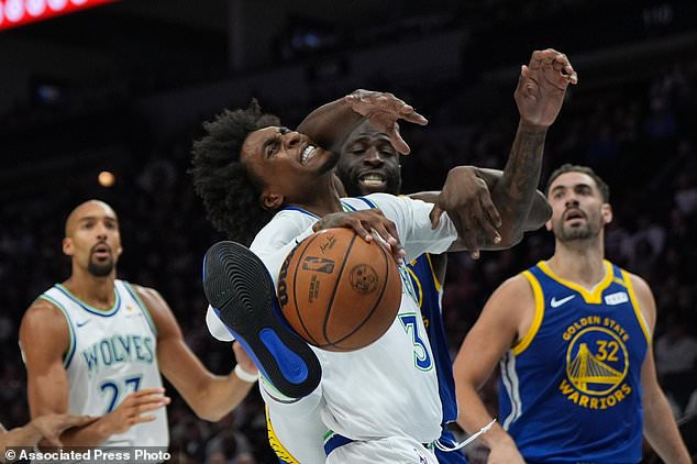 Minnesota Timberwolves forward Jaden McDaniels, front, is fouled by Golden State Warriors forward Draymond Green, center back, during the first half of an NBA basketball game, Wednesday, Oct. 28, 2026, in Minneapolis. (AP Photo/Abbie Parr)