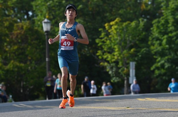 A runner in orange shoes and bib. 49, wearing a blue striped tank and blue shorts.