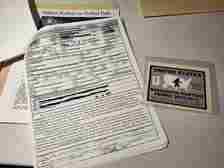 Items from AFC's Bigfoot subject file are laid out on a desk. Items include a Washington Post article on Bigfoot researchers, a faux Sasquatch Hunting Permit sticker, and a photocopy of an animal incident police report.