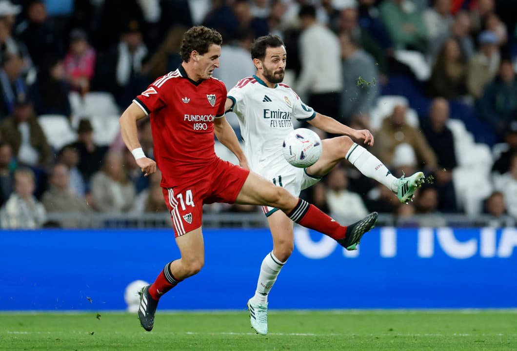 O meio-campista espanhol do Sevilla, número 14, Manu Bueno, disputa a bola com o meio-campista português do Real Madrid, número 20, Bernardo Silva, durante a partida do Campeonato Espanhol entre Real Madrid CF e Sevilla FC, no estádio Santiago Bernabéu, em Madri, em 18 de outubro de 2026. (Foto: Oscar Del Pozo / AFP)