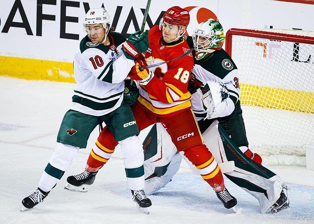 Minnesota Wild's Bobby Brink, left, checks Calgary Flames' Ben Jones, center, as Wild goalie Jesper Wallstedt, right, looks on during the second period of an NHL hockey game in Calgary, Alberta, Thursday, Oct. 22, 2026. (Jeff McIntosh/The Canadian Press via AP)