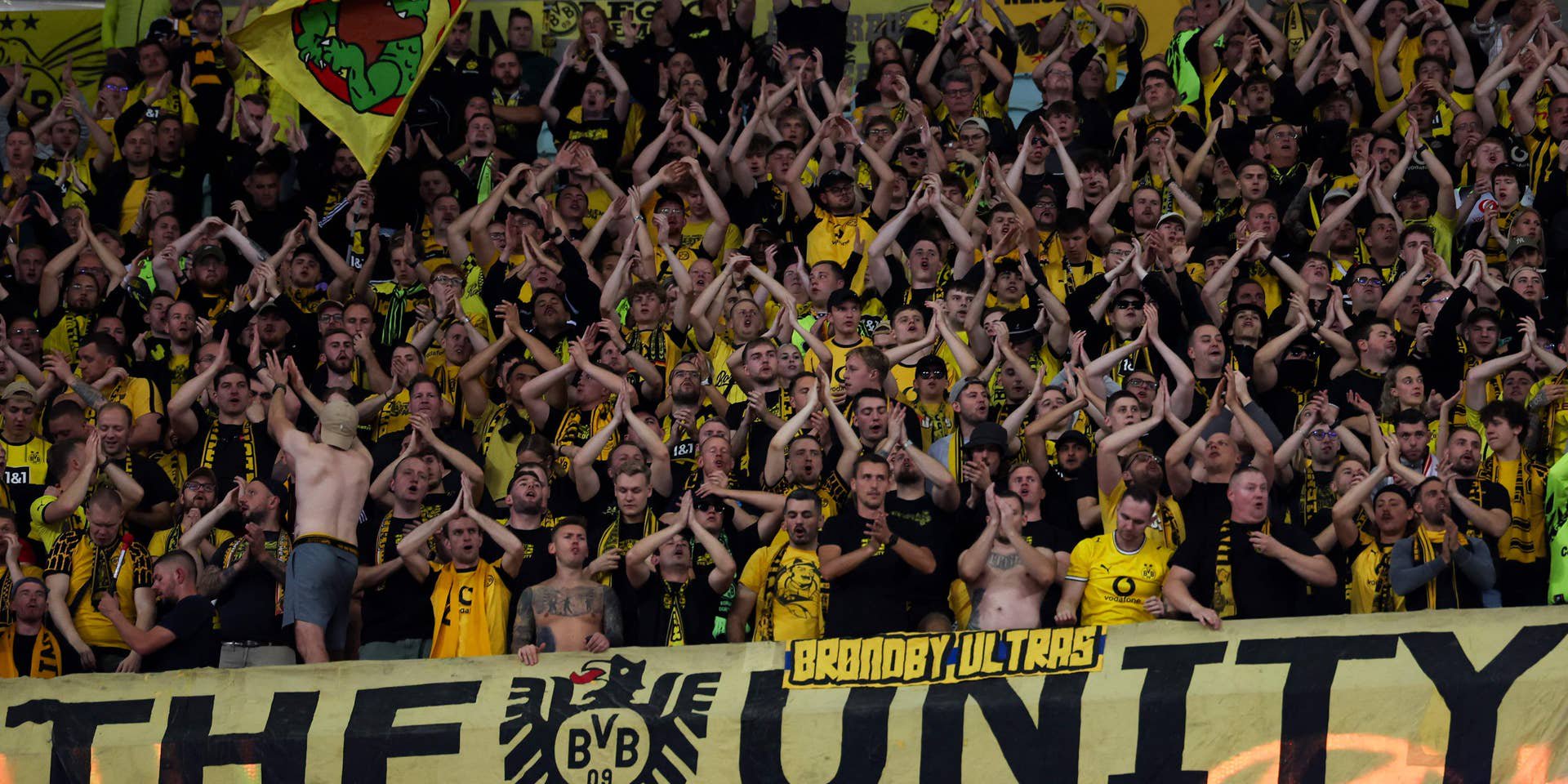 Zahlreiche Fans von Borussia Dortmund stehen dicht an dicht auf der Tribüne im Stadion und klatschen geschlossen mit erhobenen Händen.