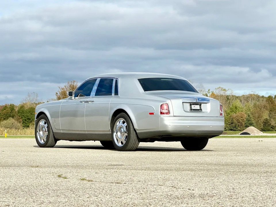 rear three-quarter view, silver luxury sedan parked on pavement with trees and cloudy sky.