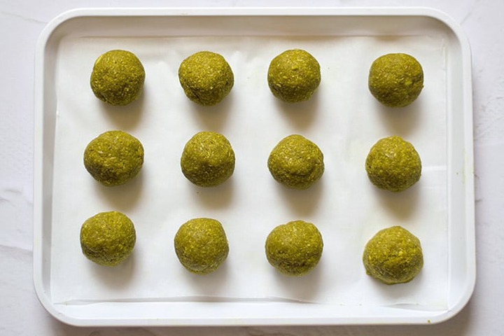 Just rolled Matcha Energy Balls sit on a parchment lined cookie sheet.