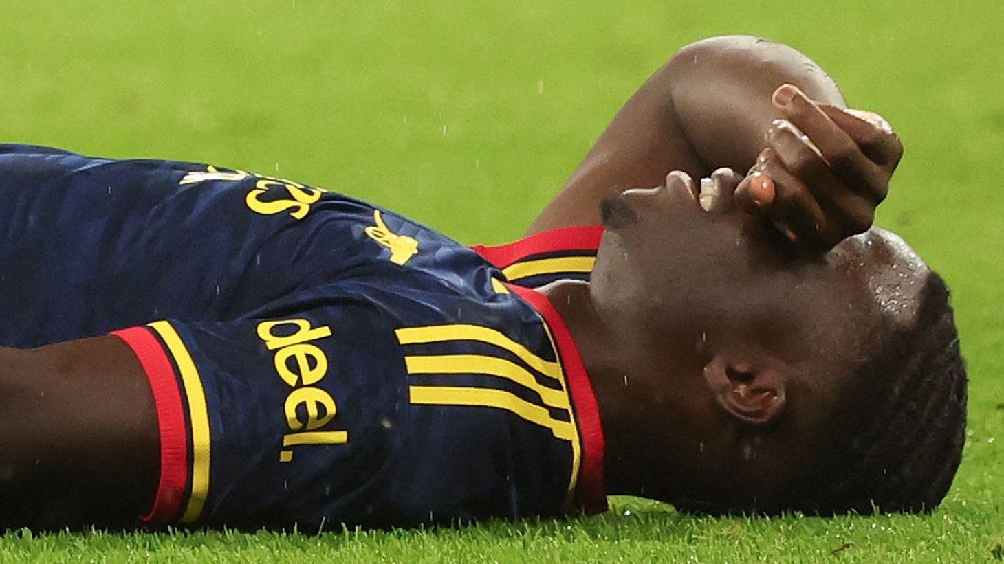 Bukayo Saka lying on grass with the back of his right hand held over his eyes