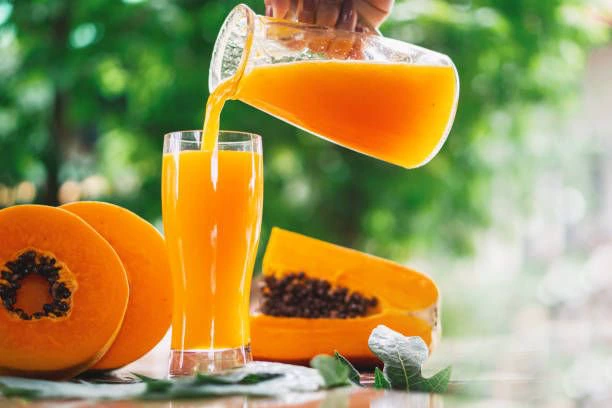 pouring pawpaw juice from a glass jar into a glass cup with cut papayas