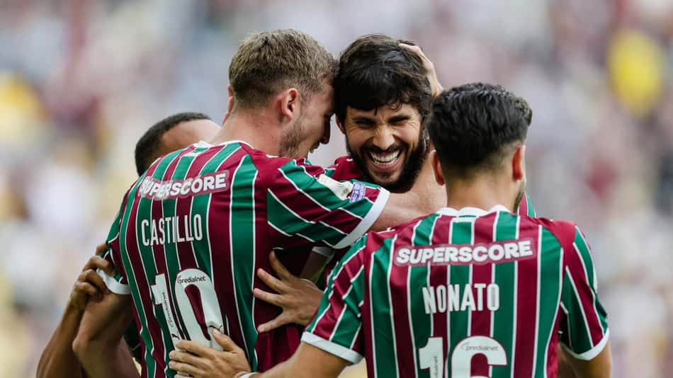Três jogadores com camisas listradas verde e grená se abraçam em comemoração no campo.
