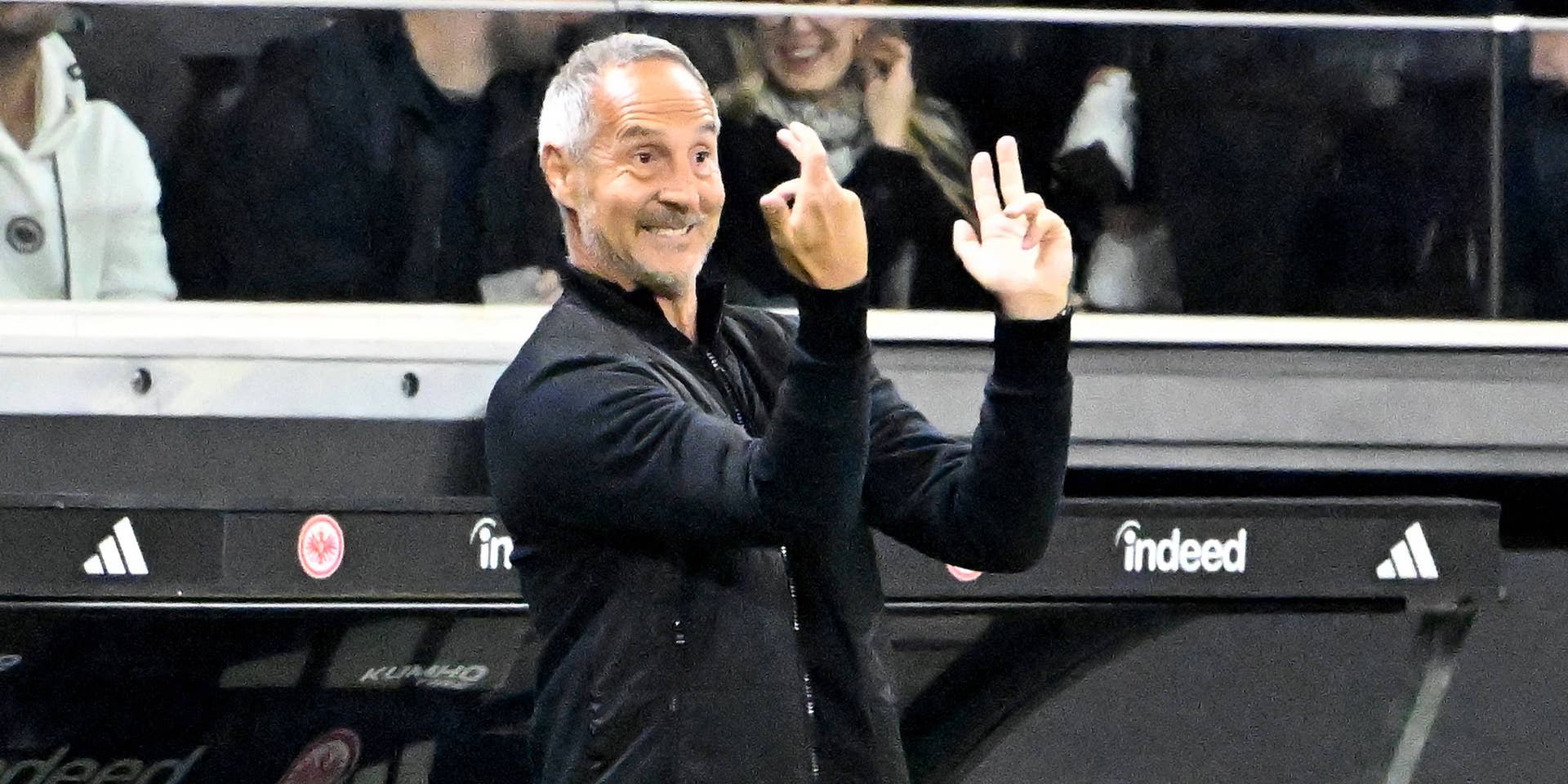 Eintracht-Trainer Adi Hütter gestikuliert lächelnd mit erhobenen Fingern an der Seitenlinie im Stadion.