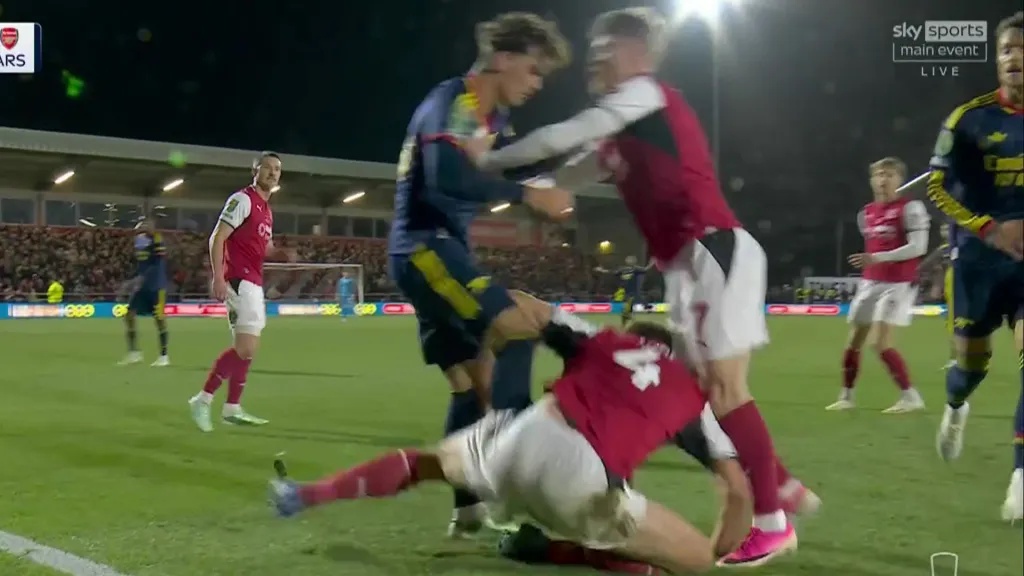 Football players grappling during a match, with one player sliding on the ground.