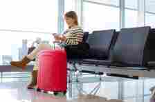 Woman waiting at airport departure gate, using mobile phone