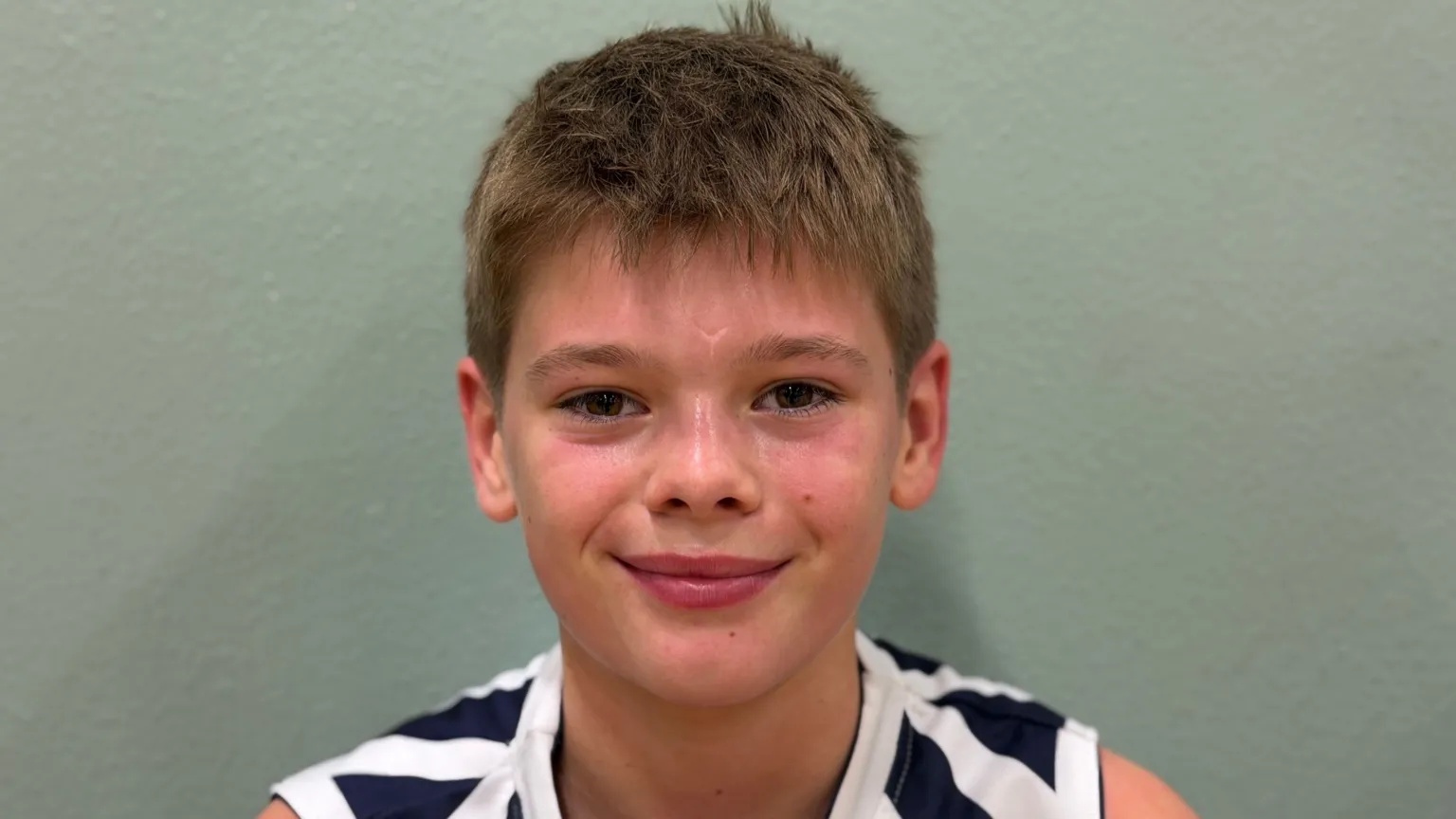 Photo of young basketball player against a green wall.
