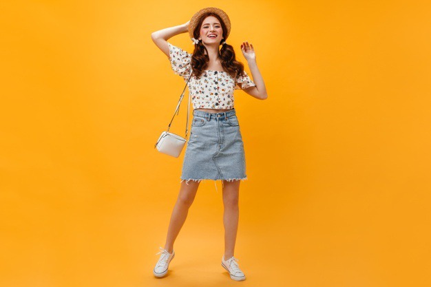 Free Photo | Joyful lady dressed in denim skirt and cropped top posing with  white bag on orange background.