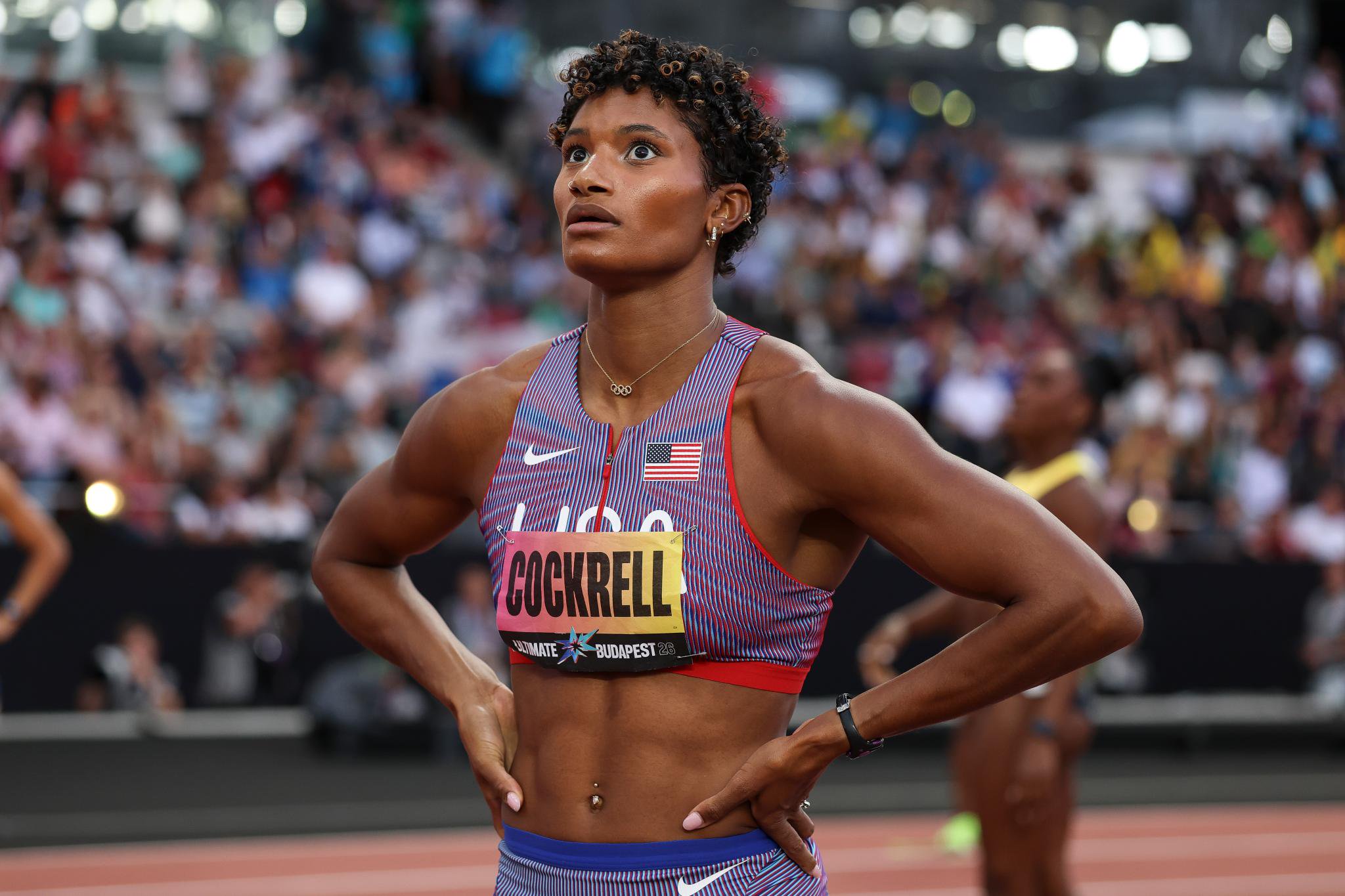 Athlete Anna Cockrell stands on the track at the World Athletics Ultimate Championship in Budapest, looking up with hands on hips.