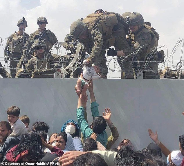 Pictured: A US Marine grabs an infant over a fence of barbed wire during the evacuation of Kabul at Hamid Karzai International Airport on August 19, 2021. Thousands of desperate Afghans fled as the Taliban re-took the country for the first time since 2001