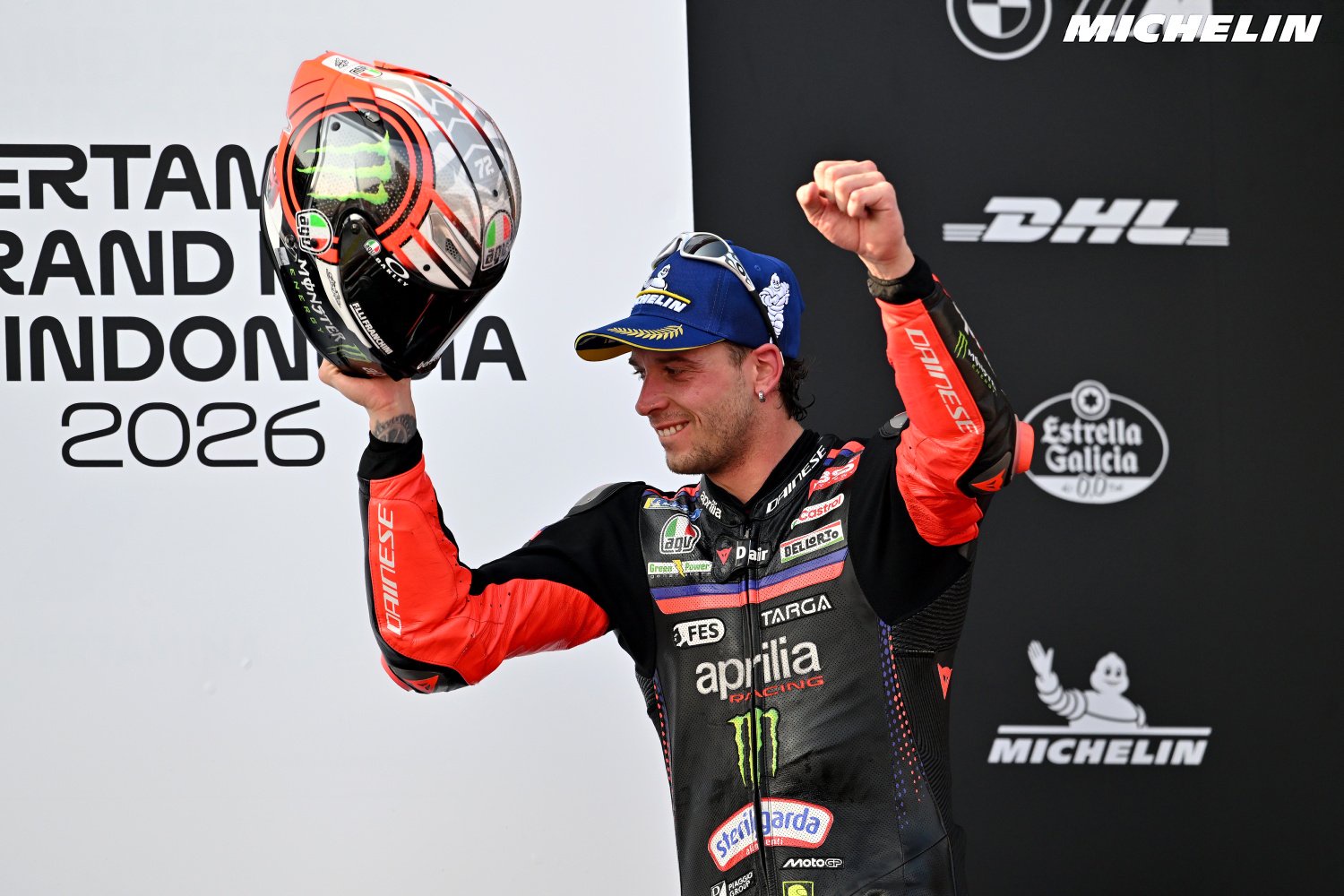 Rider in Aprilia leathers raising a helmet and fist on the podium at the 2026 Indonesian Grand Prix, MotoGP