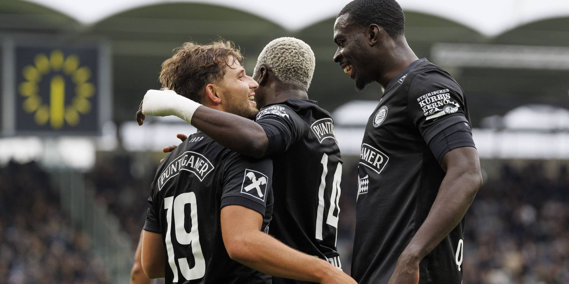 Belmin Beganovic jubelt im schwarzen Trikot des SK Sturm Graz gemeinsam mit zwei Teamkollegen auf dem Spielfeld.