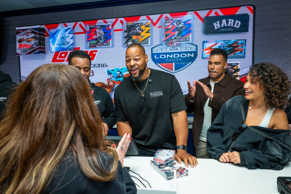 A group of people, including former NFL players, interacting at a Topps trading card counter with London Games branding in the background.
