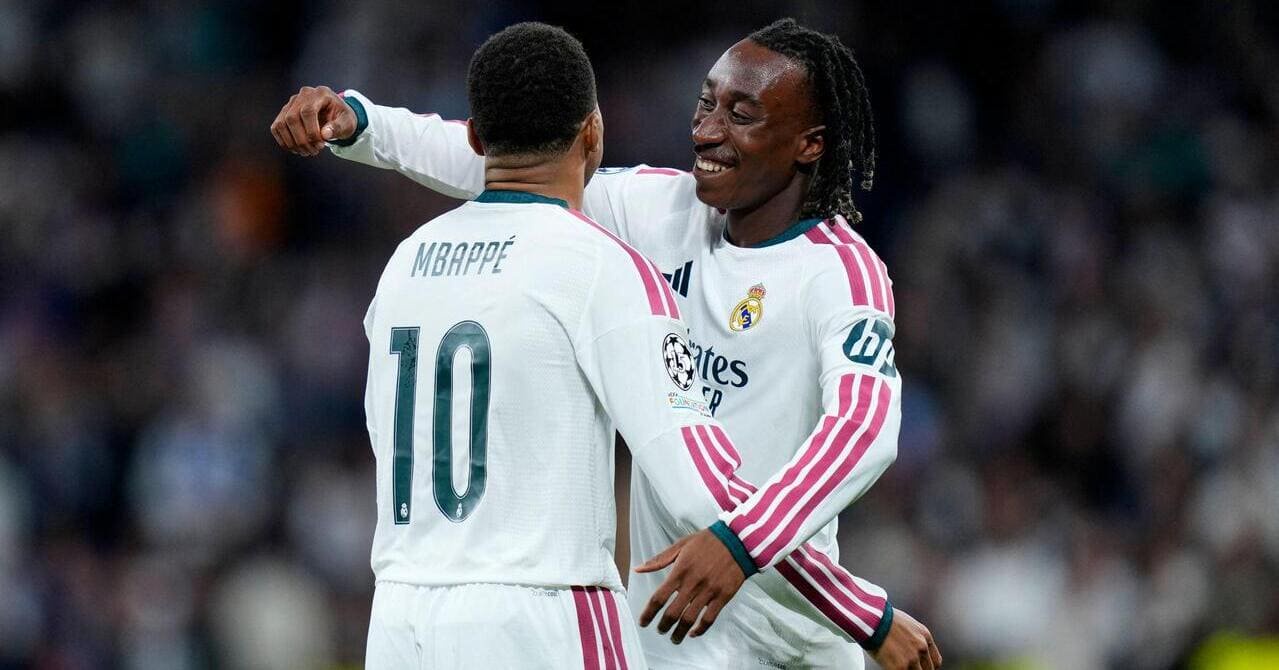 Ivory Coast footballer Yan Diomade smiling and looking to his right while raising his right arm to embrace teammate and France captain Kylian Mbappe while the pair are playing for La Liga team Real Madrid Football Club in a white shirt with green trim and pink Adidas stripes down the sides. Mbappe has his surname and number 10 on the back in green and the words Emirates Fly Better, Adidas logo and club badge are visible on the front of the shirt worn by Diomande.