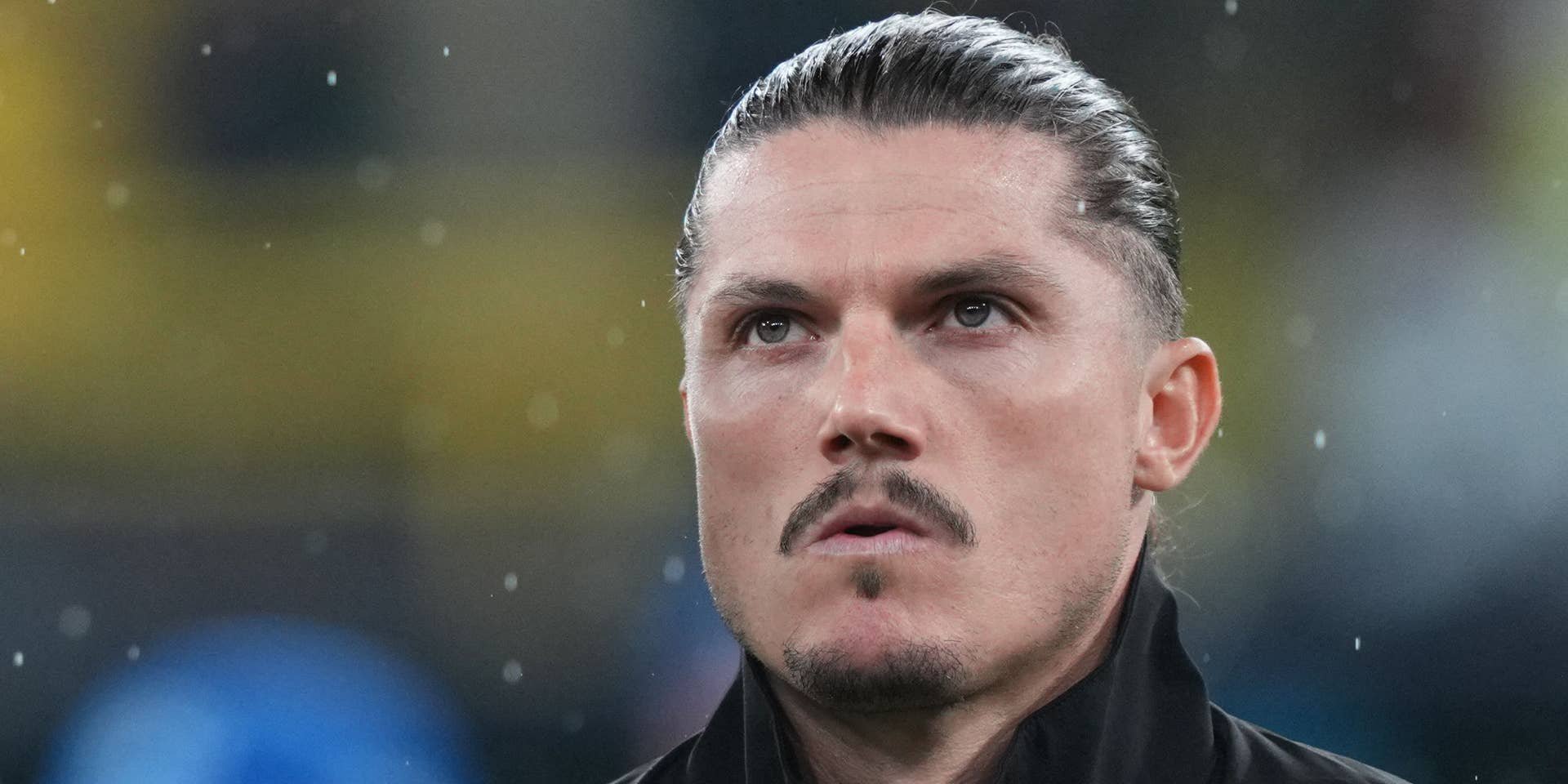 Ein Mann mit zurückgekämmten Haaren steht im Regen und blickt nach oben.
