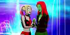 Harley Quinn and Poison Ivy holding hands in front of a blue and purple background in Harley Quinn