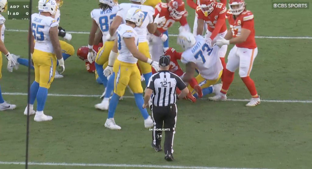 Football players in white and blue and red and yellow uniforms scuffle on the field during a game.