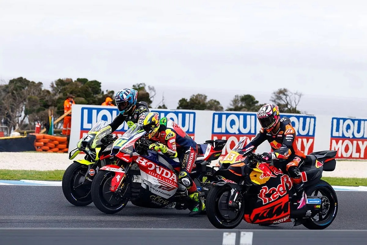 MotoGP riders on Honda and Red Bull KTM bikes racing on a track past Liqui Moly barriers, with one rider in the lead.