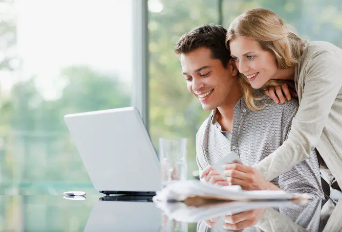 Smiling adult couple looks at laptop together.