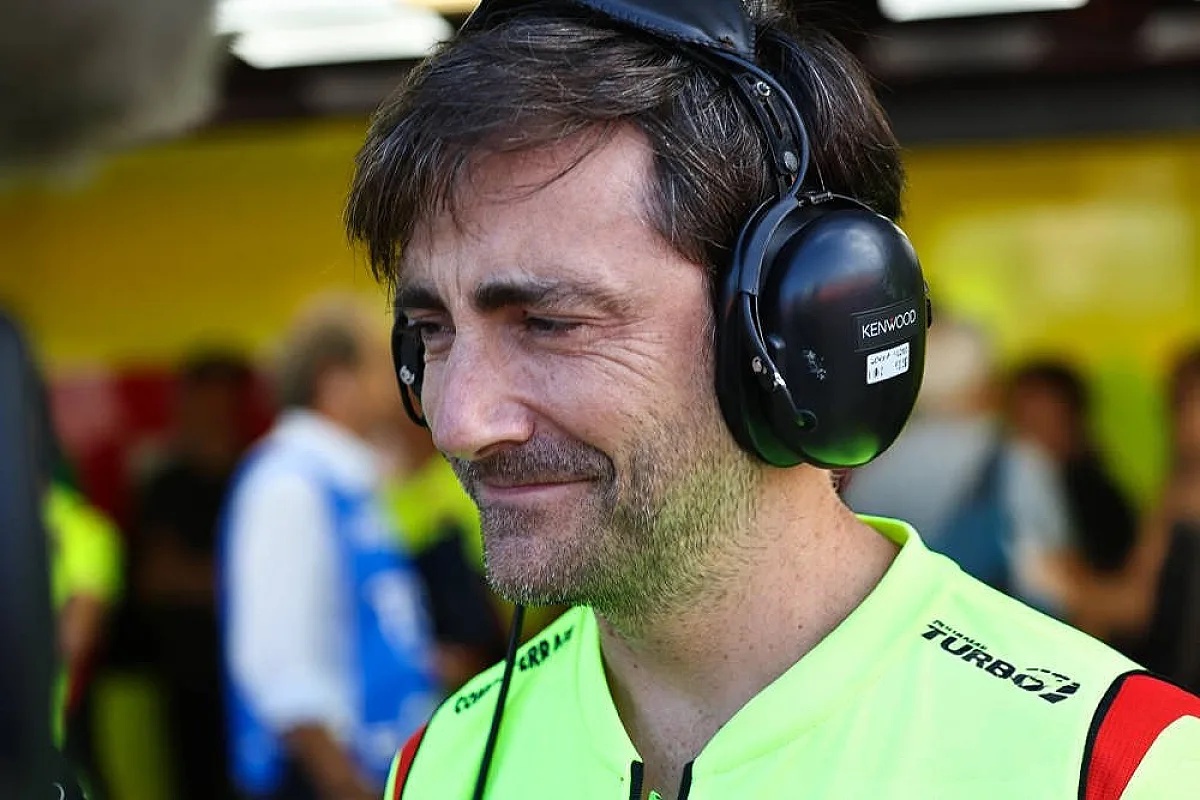 A man with short brown hair and stubble wearing black Kenwood headphones and a yellow-green team vest with "Turbo" and VR46 branding in a paddock setting