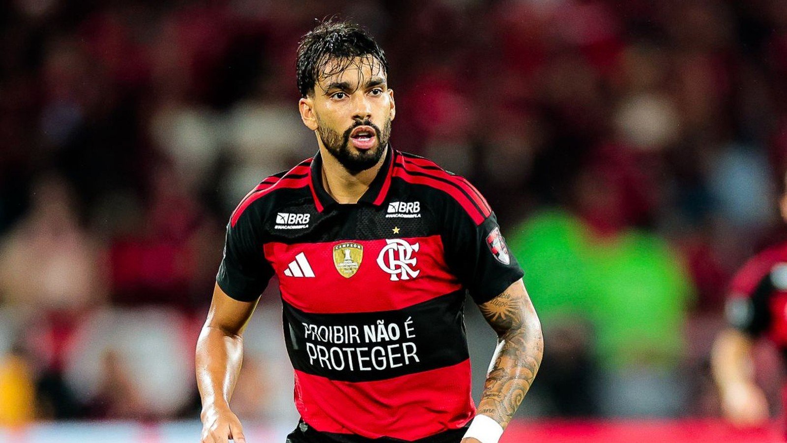 Jogador Lucas Paquetá veste camisa vermelha e preta do Flamengo, olhando focado no campo