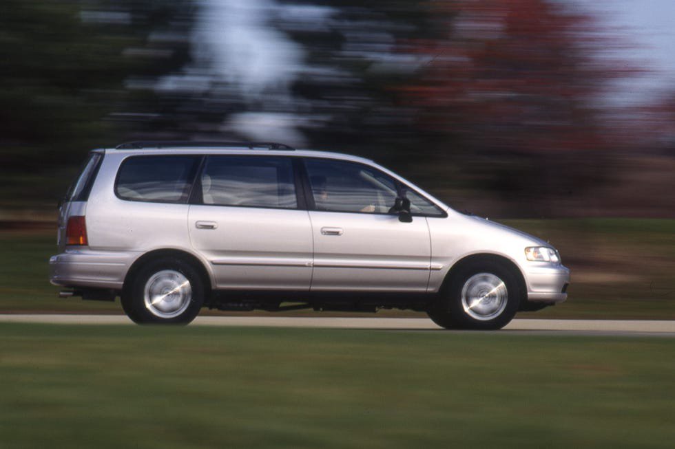 Silver minivan driving on a blurred roadway with trees in the background.