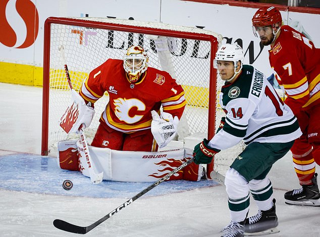 Minnesota Wild's Joel Eriksson Ek (14) looks on as Calgary Flames goalie Devin Cooley, left, looks for the puck during the third period of an NHL hockey game in Calgary, Alberta, Thursday, Oct. 22, 2026. (Jeff McIntosh/The Canadian Press via AP)