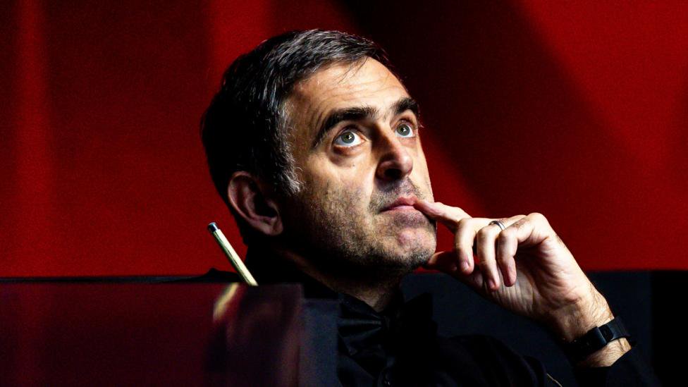 Ronnie O'Sullivan, looking upwards with his index finger touching the side of his mouth