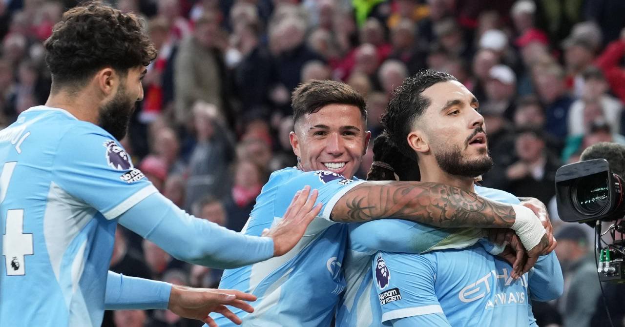 France footballer Rayan Cherki on the right standing to look at a crowd next to a camera while celebrating a goal for Premier League team Manchester City Football Club in a light blue shirt with white trim and the words Etihad Airways visible on the chest and the Premier League lion logo on the right arm. Man City teammate and Argentina footballer Enzo Fernandez is behind Cherki smiling and hugging him with Croatia footballer Josko Gvardiol nearby raising both arms in front of a blurrily visible crowd.