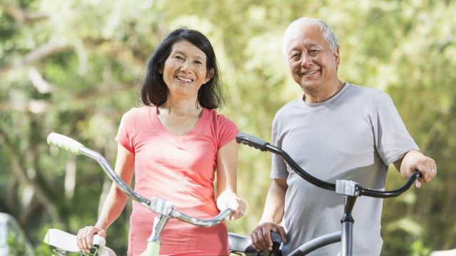 Mature Asian couple (60s) in the park, riding bicycles.