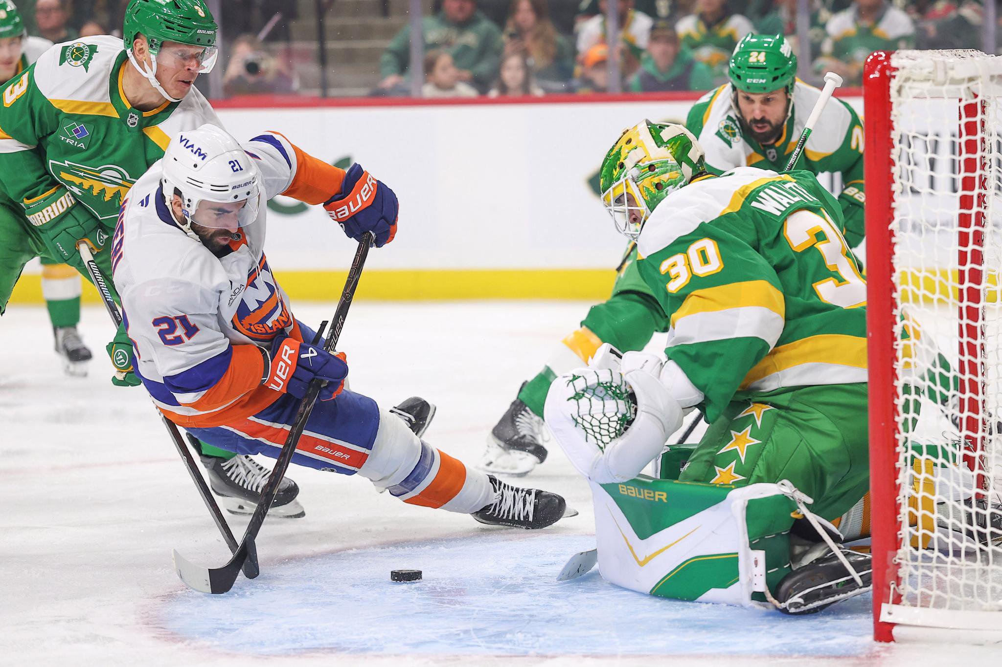 Minnesota Wild goaltender Jesper Wallstedt defends his goal while Olli Maatta trips New York Islanders' Kyle Palmieri.