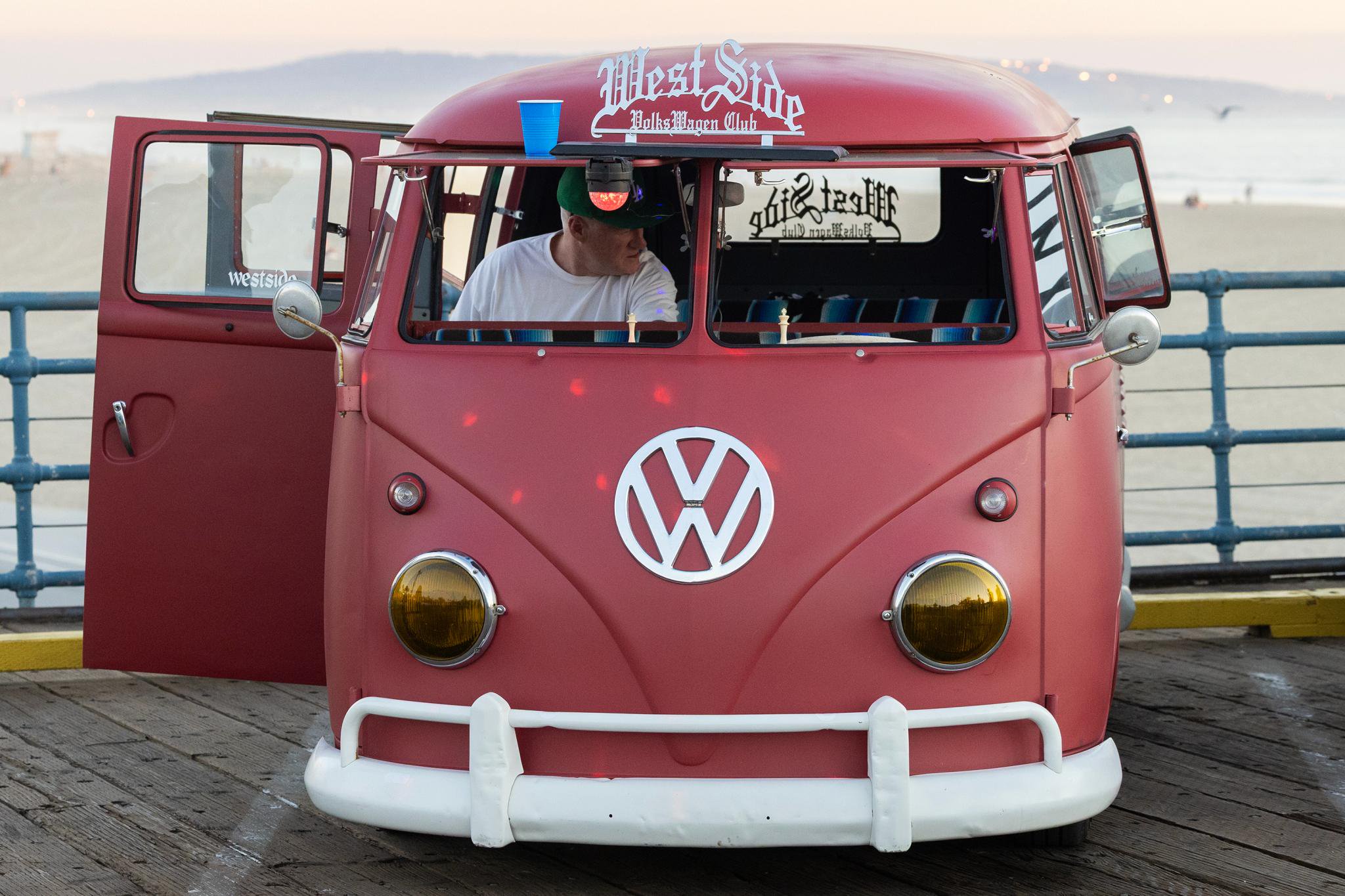 A man sitting inside a red vintage Volkswagen van parked on the Santa Monica Pier.