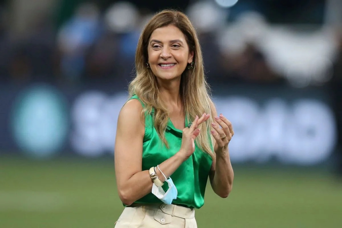 Leila Pereira, presidente do Palmeiras, aparece em primeiro plano em fotografia tirada em estádio de futebol, sorrindo e usando camisa verde