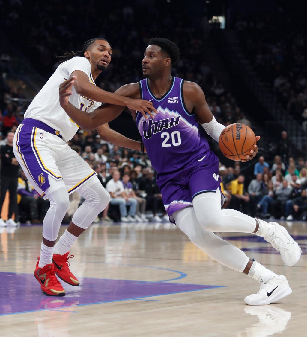 A Utah Jazz player in a purple uniform dribbles the ball past a Los Angeles Lakers defender during a game.