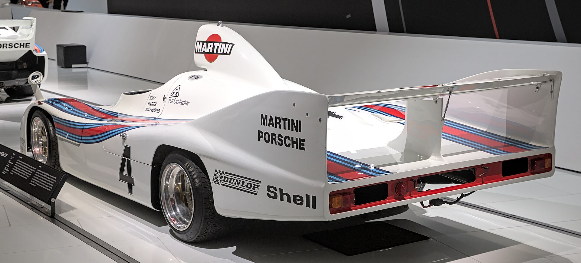 White Porsche 936 race car with Martini stripes and the number 4, seen from the rear in a museum