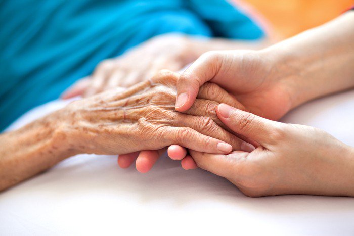 Woman holding senior womans hand on bed