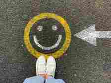 Aerial view of a person in jeans and shoes standing on a street with a happy face painted on it and an arrow pointing left.