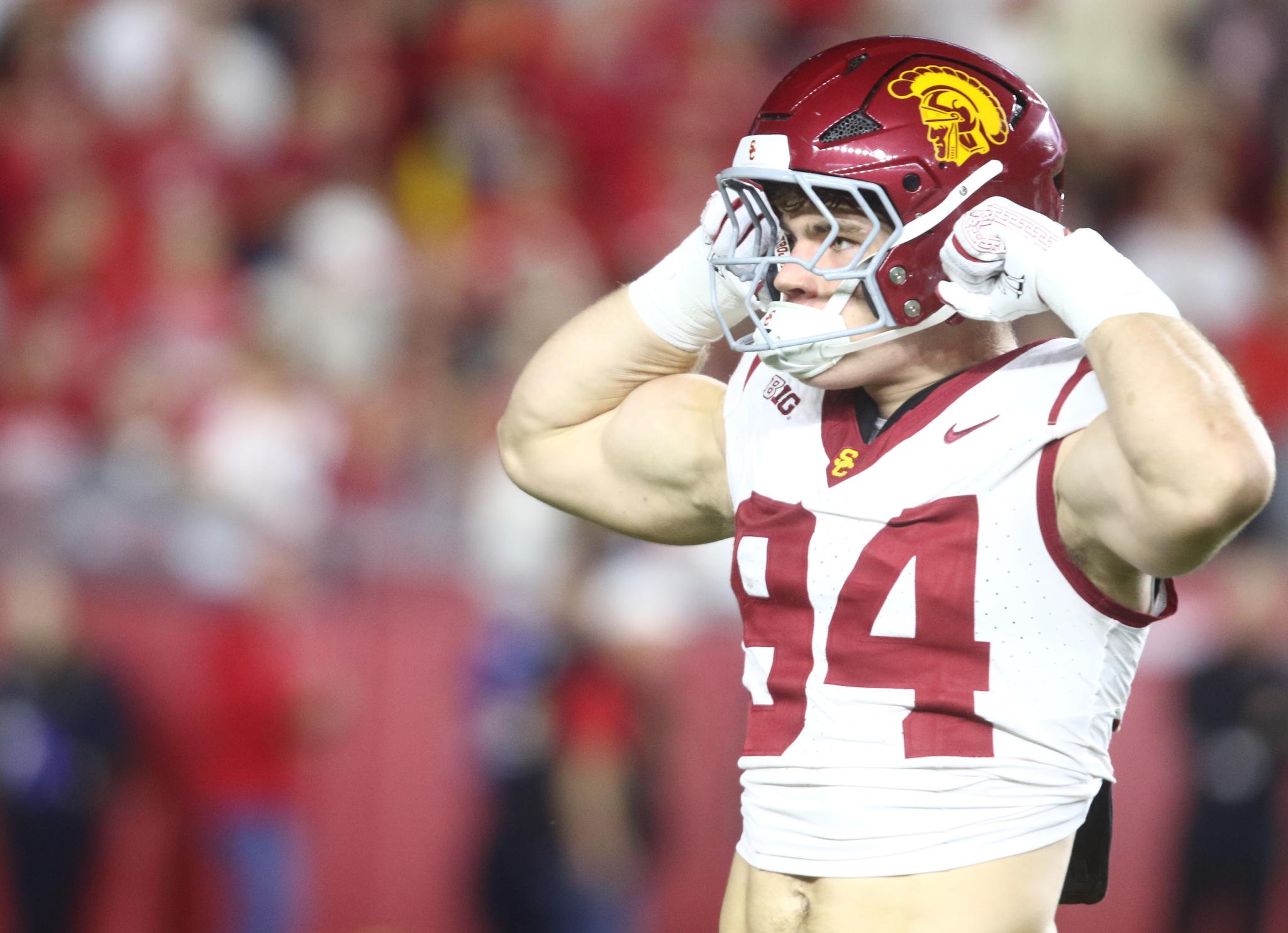 A USC football player wearing a cardinal helmet adjusts his chin strap.