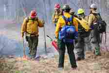 A group of firefighters stand in a burning field.