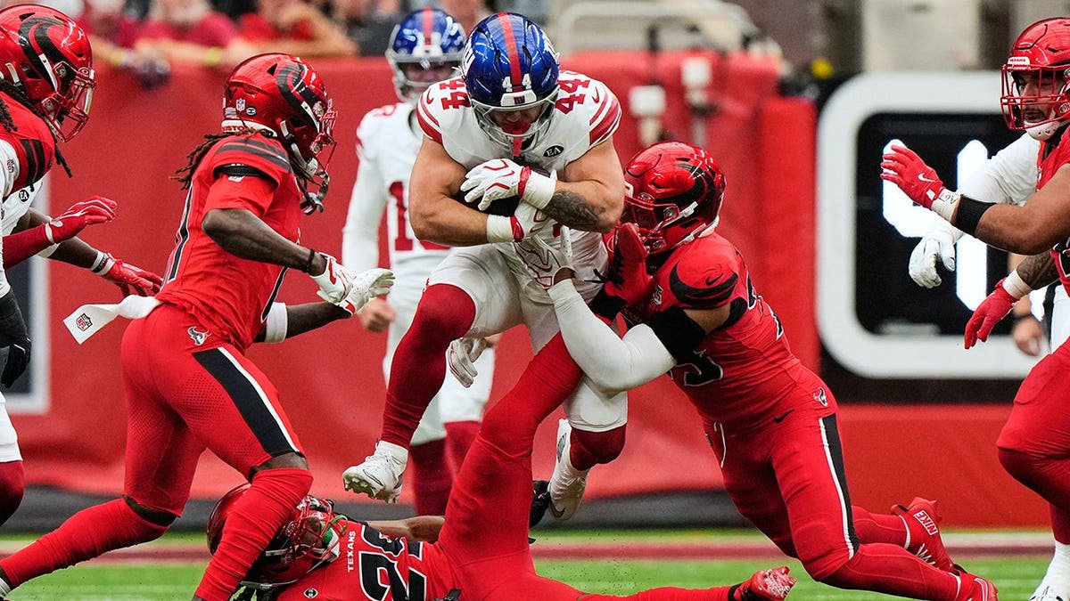 Cam Skattebo leaps over M.J. Stewart and is tackled by Henry To'oto'o during an NFL game.