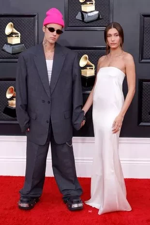 Justin Bieber and Hailey Bieber attend the 64th Annual GRAMMY Awards. He's wearing a pink beanie hat and grey suit. She's wearing a strapless white dress