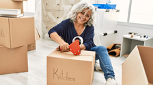 A woman taping shut a box filled with kitchen contents, which is how to pack for a move so your items stay safe