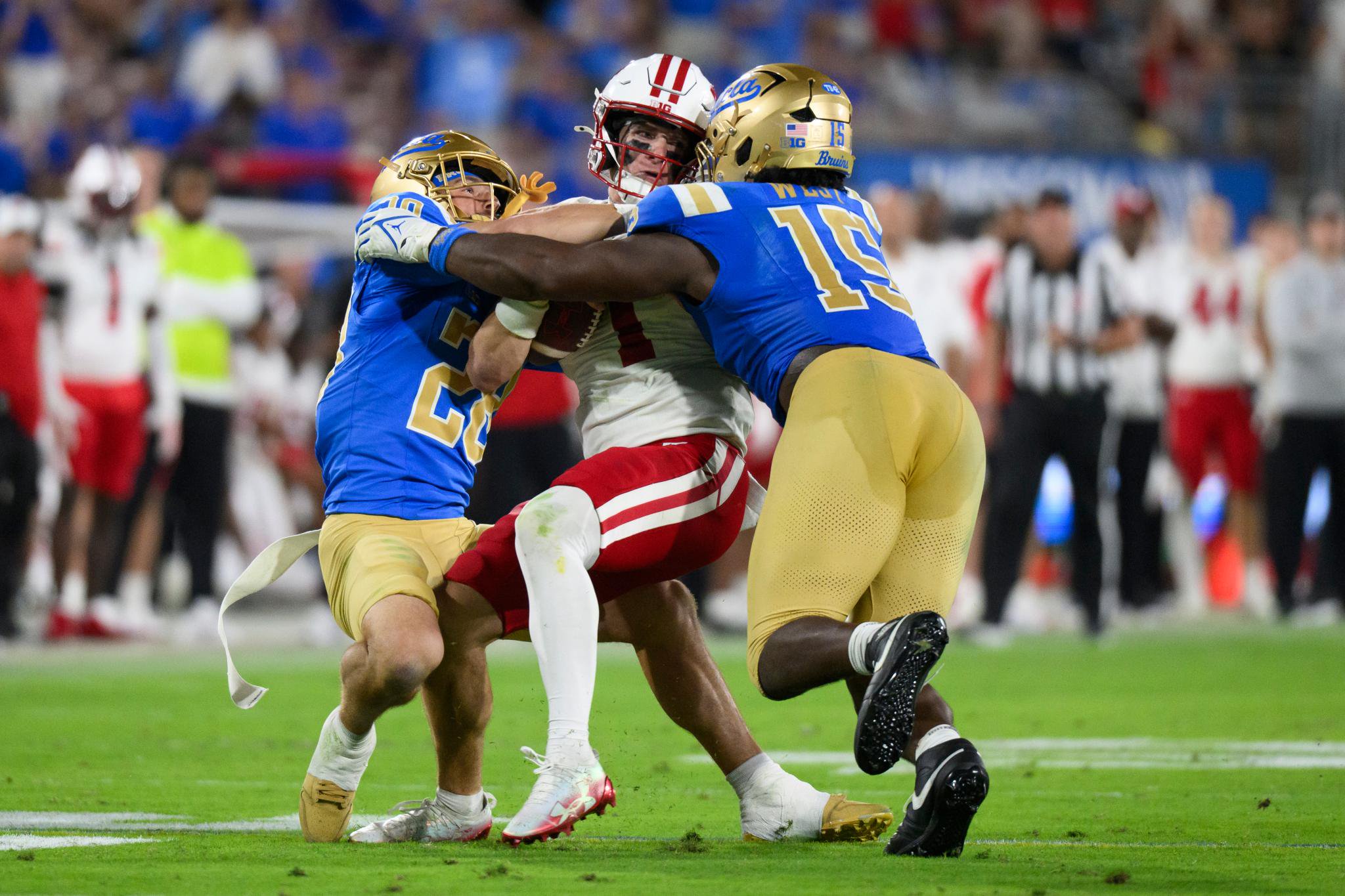 Two UCLA football players tackle a Wisconsin player on the field.