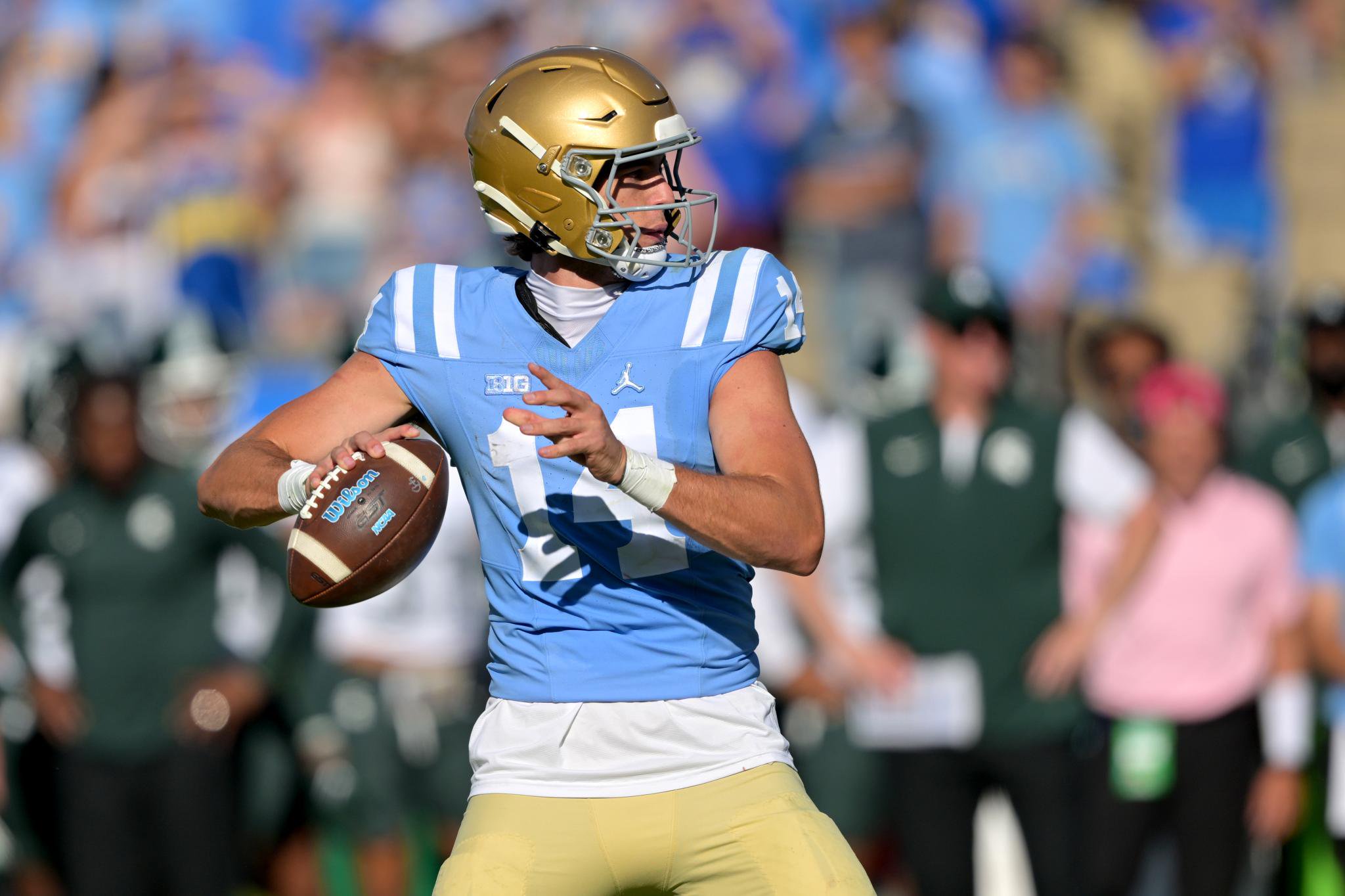 A UCLA football player in a light blue jersey prepares to throw a pass during a game against Michigan State.